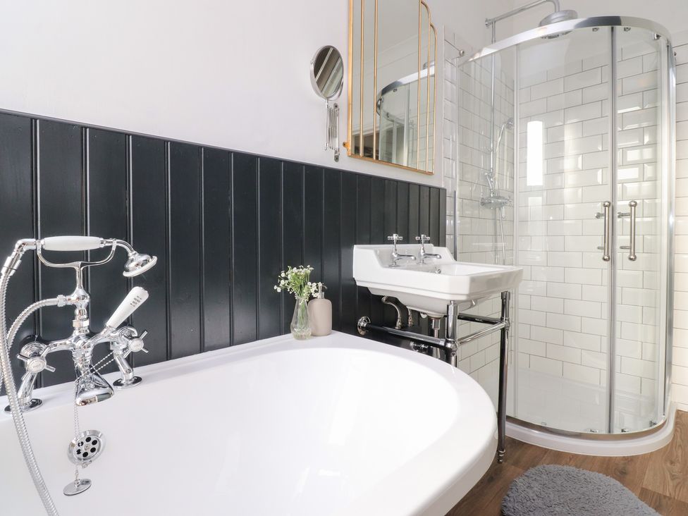 A bathroom with a bathtub, shower, sink, and mirror at Heathcliff Cottage