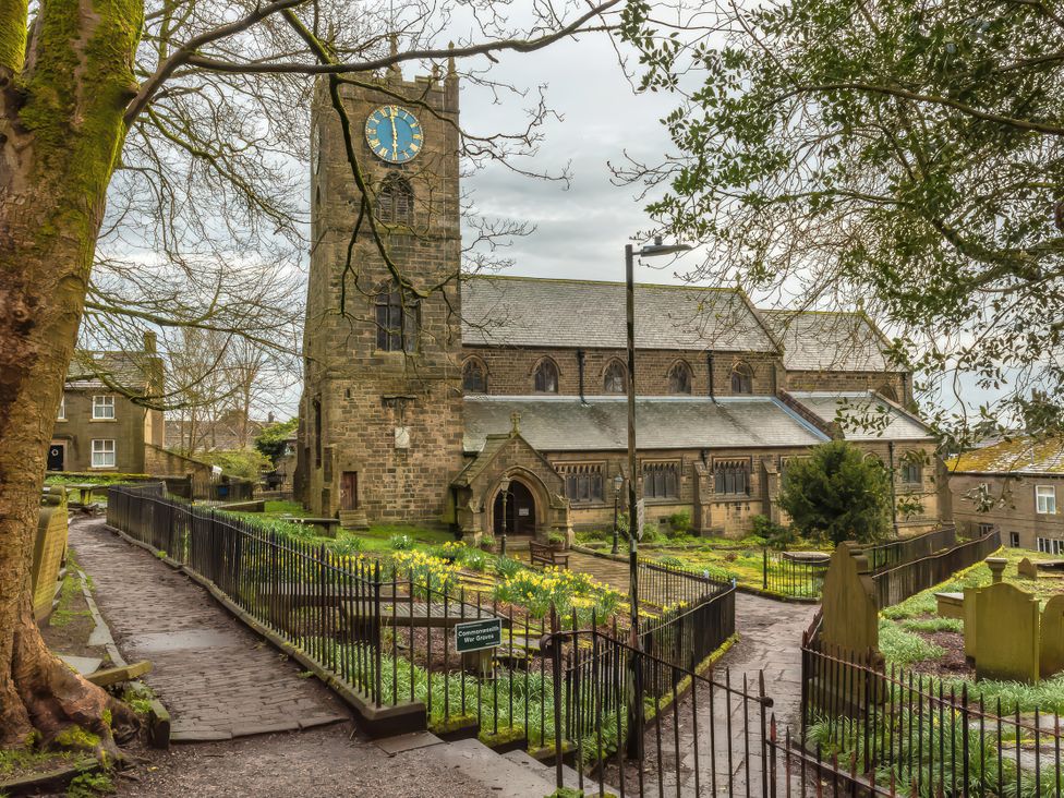 A church with a clock tower and a pathway surrounded by flowers at Heathcliff Cottage in Haworth