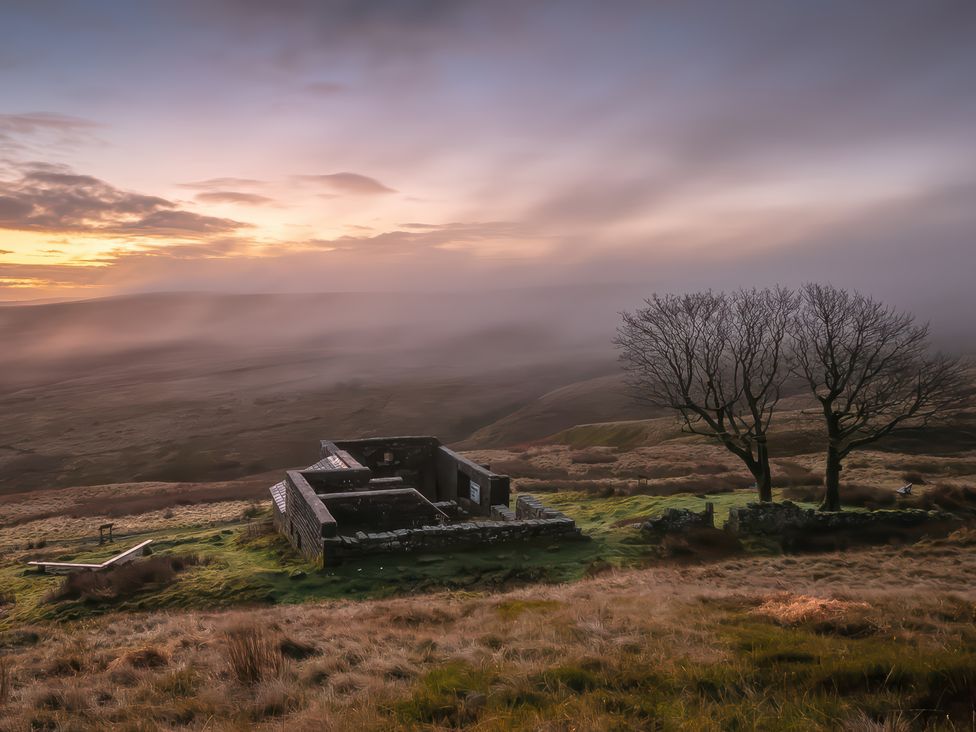 A ruined building and trees on a grassy hillside at Heathcliff Cottage in Haworth