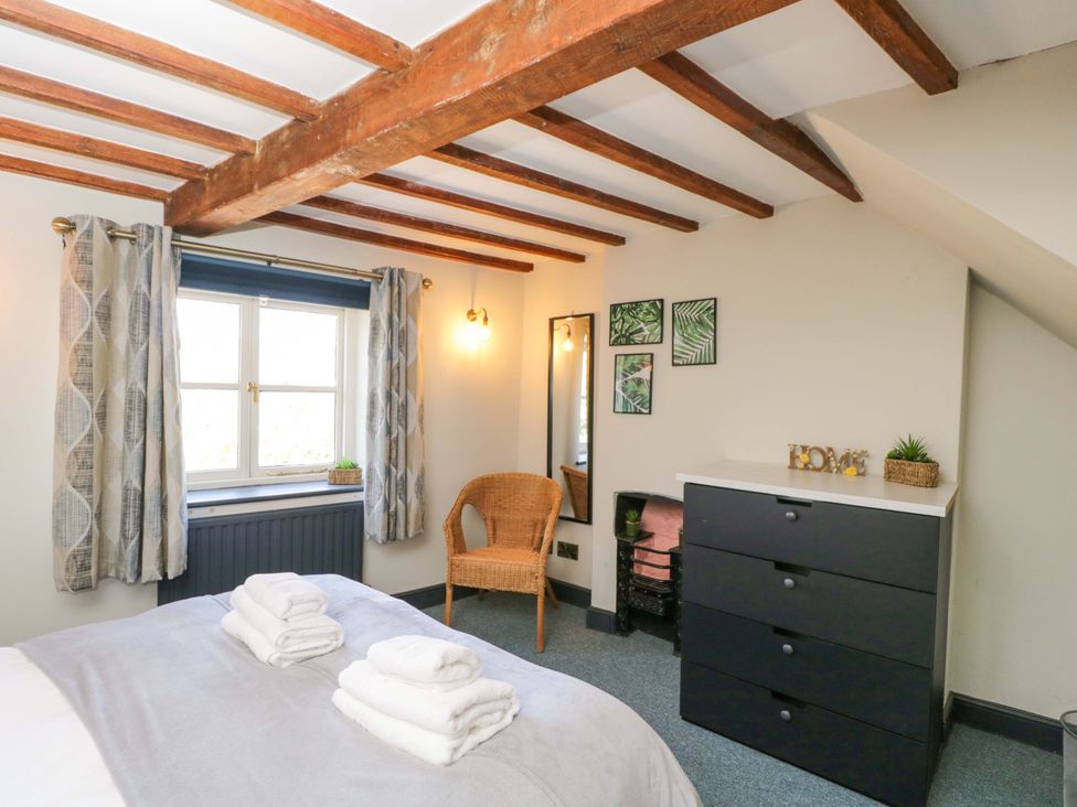 A bedroom with a bed, window, chair, drawers and wall art at Elm Cottage in Moreton-In-Marsh