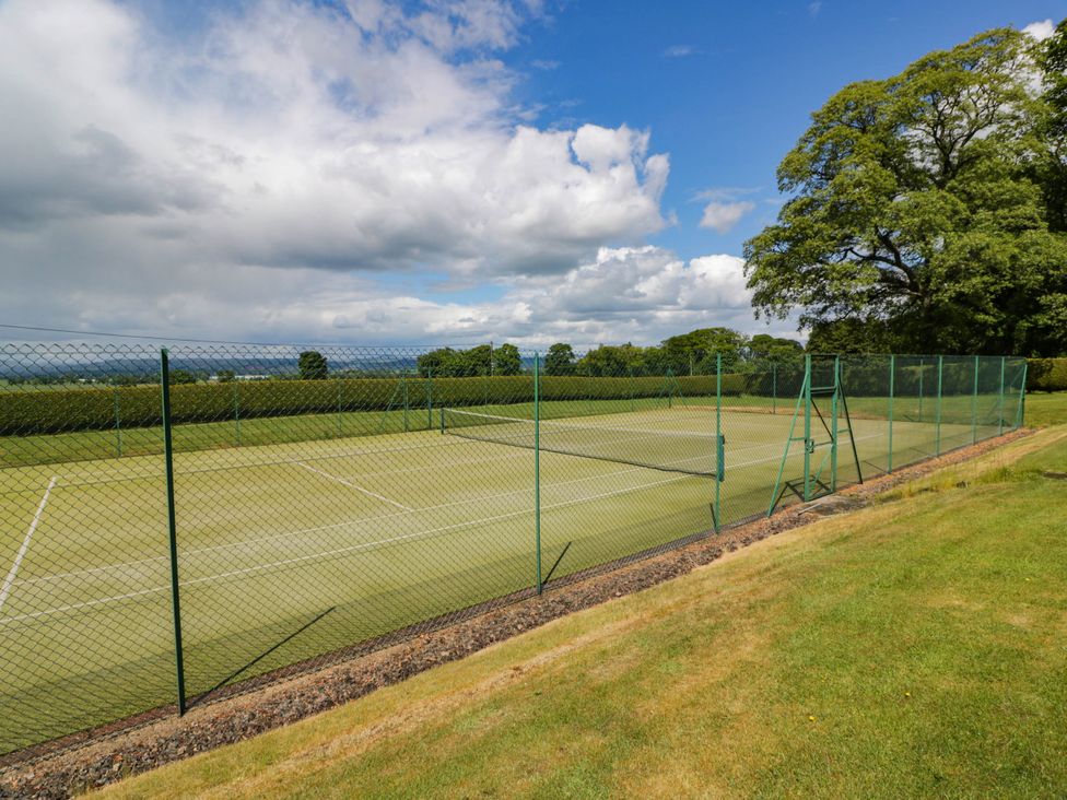 A tennis court with a fence and grass area at Eagle Glen Manor House in Blairgowrie