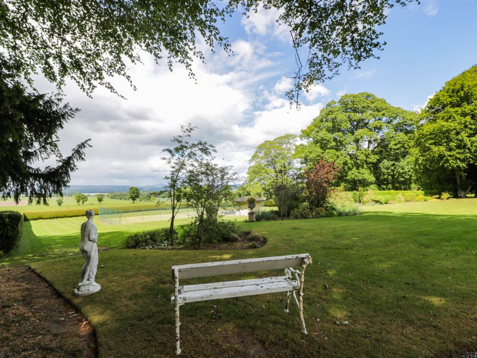 A garden with a bench, statue, and tennis court at Eagle Glen Manor House in Blairgowrie