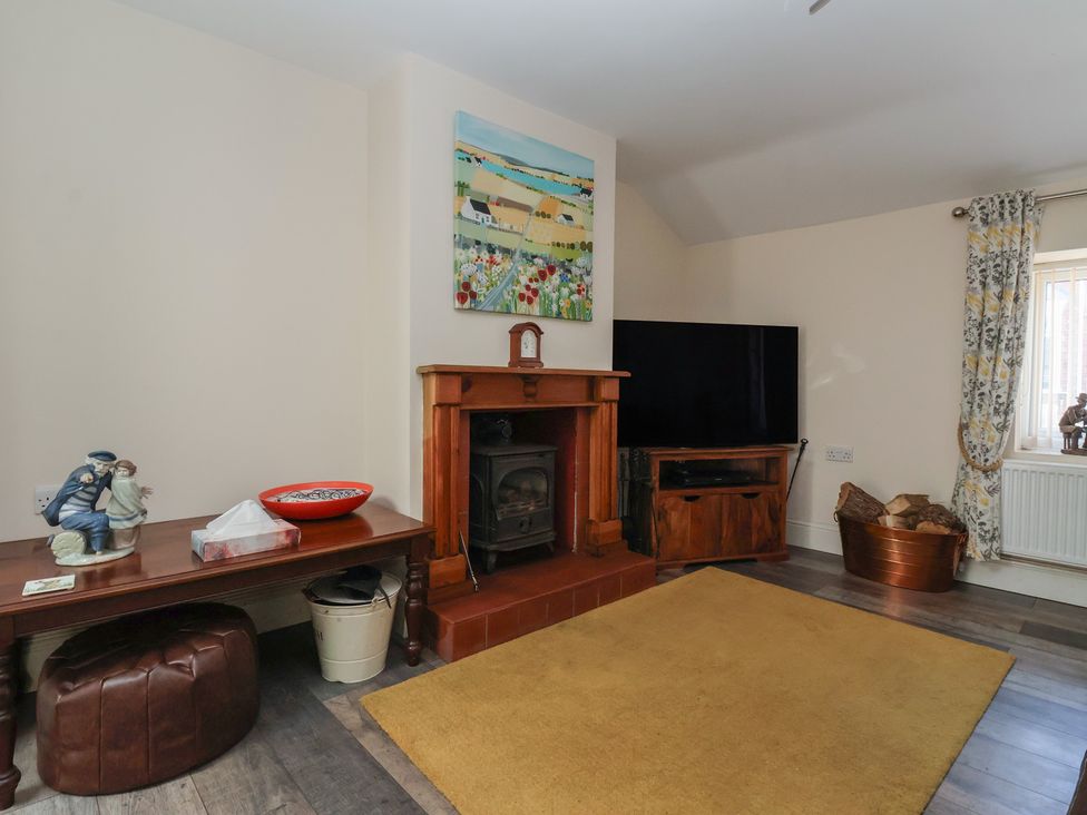 A living room with a wooden fireplace a television on a wooden stand a brown leather stool and a yellow rug at 4 Queen Street in Withernsea