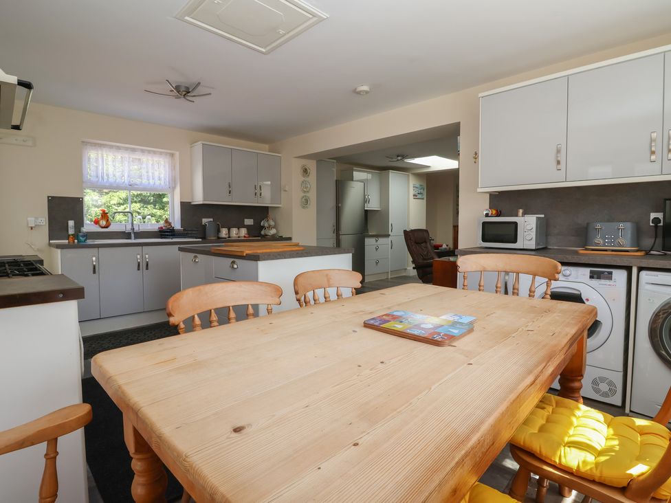 A kitchen with a wooden dining table and chairs with yellow cushions a microwave toaster washing machine and fridge at 4 Queen Street in Withernsea