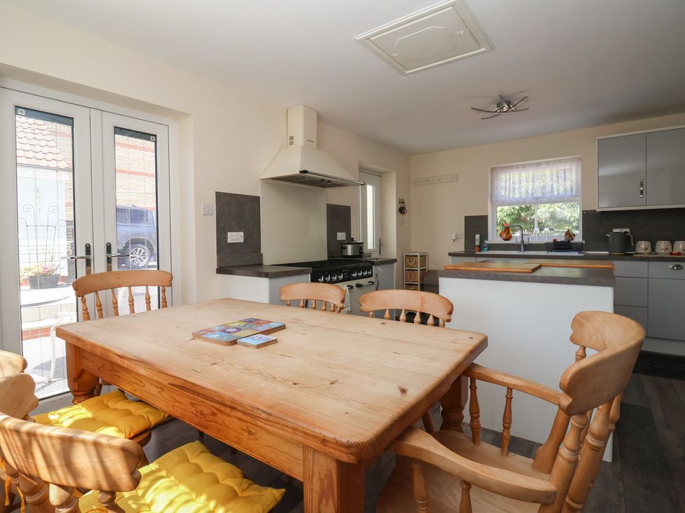 A kitchen with wooden dining table and chairs yellow cushions stove and sink by window at 4 Queen Street in Withernsea