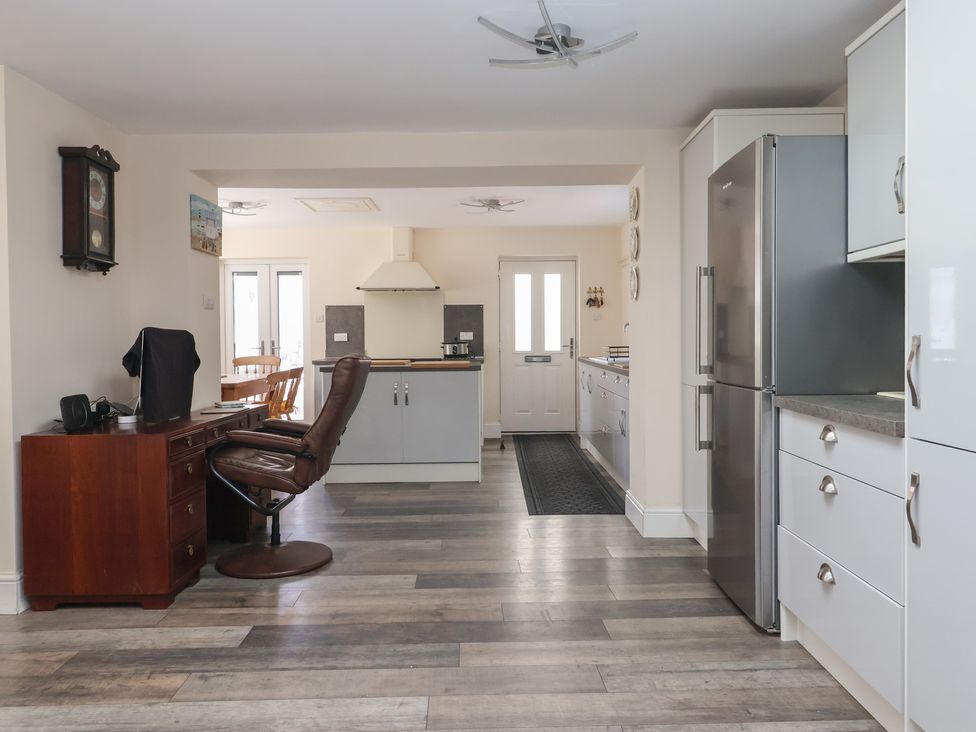 A kitchen with white cabinets a stainless steel refrigerator a wooden desk with a chair and a dining area visible at 4 Queen Street in Withernsea