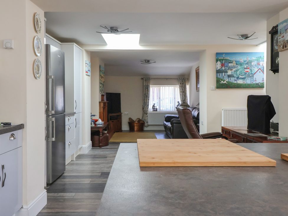 A kitchen area with a cutting board on the counter leading to a living room with sofas tv and paintings at 4 Queen Street in Withernsea