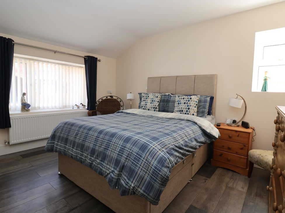A bedroom with a bed with blue plaid bedding two wooden bedside tables and a window with vertical blinds at 4 Queen Street in Withernsea