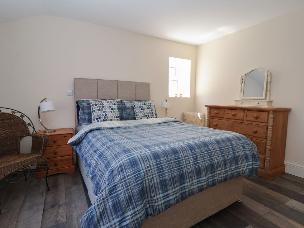 A bedroom with a bed with blue plaid bedding a wooden dresser with a mirror a wicker chair and a wooden nightstand with a lamp at 4 Queen Street in Withernsea