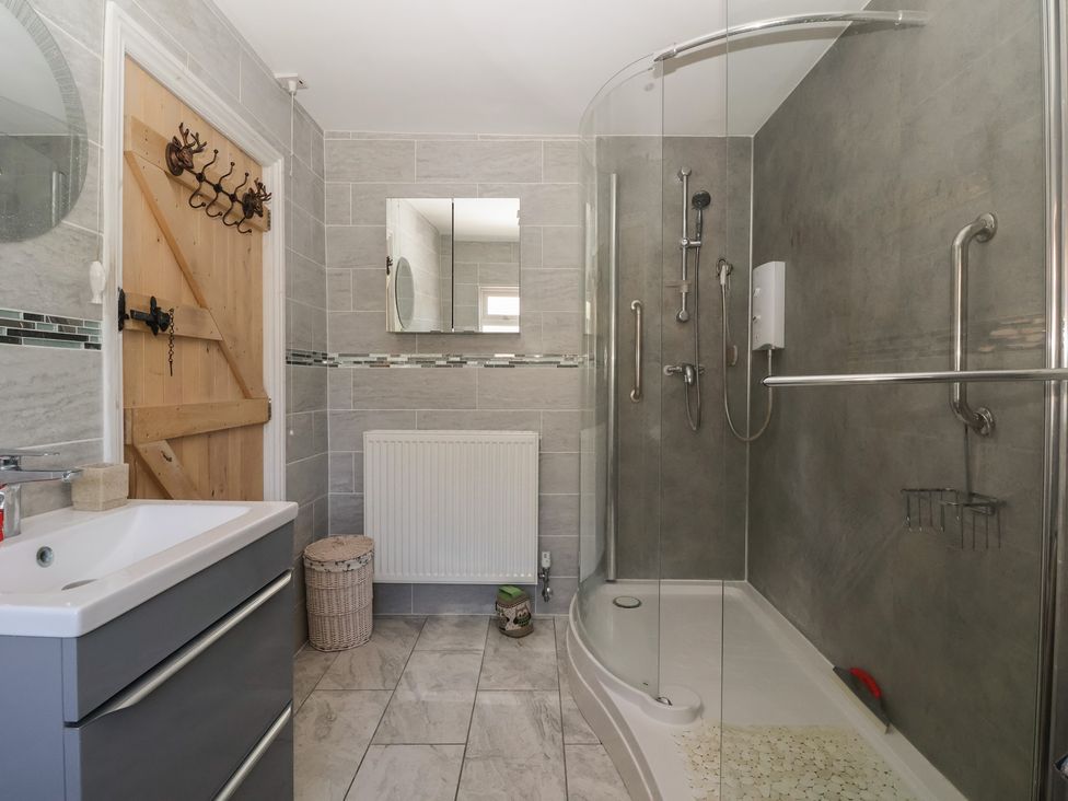 A bathroom with a shower enclosure a sink with cabinet a wooden door and a wall mirror at 4 Queen Street in Withernsea