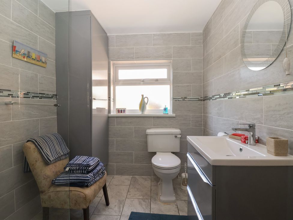 A bathroom with a toilet a sink with storage a window a chair with towels and a tall cabinet at 4 Queen Street in Withernsea