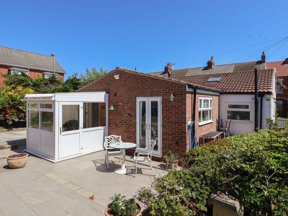 A backyard patio area with a small table and two chairs next to a brick house with a white enclosed porch at 4 Queen Street in Withernsea