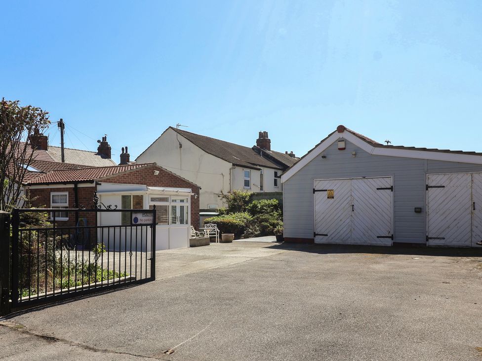 An outdoor area with a black metal gate two small buildings with white doors and a concrete driveway at 4 Queen Street in Withernsea