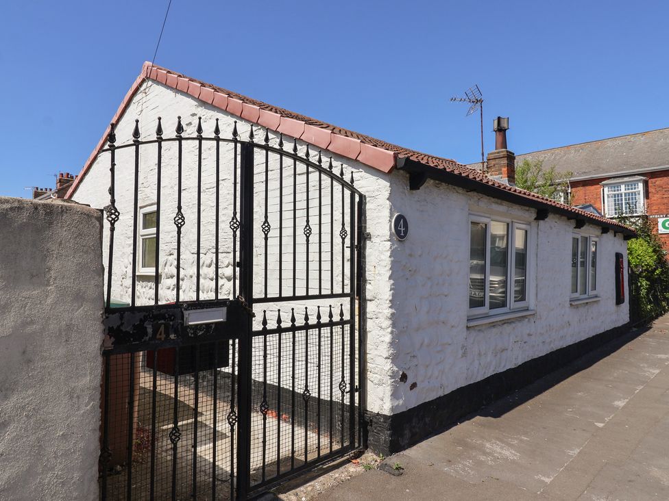 A white single-story building with a tiled roof behind a black metal gate on a sidewalk at 4 Queen Street in Withernsea