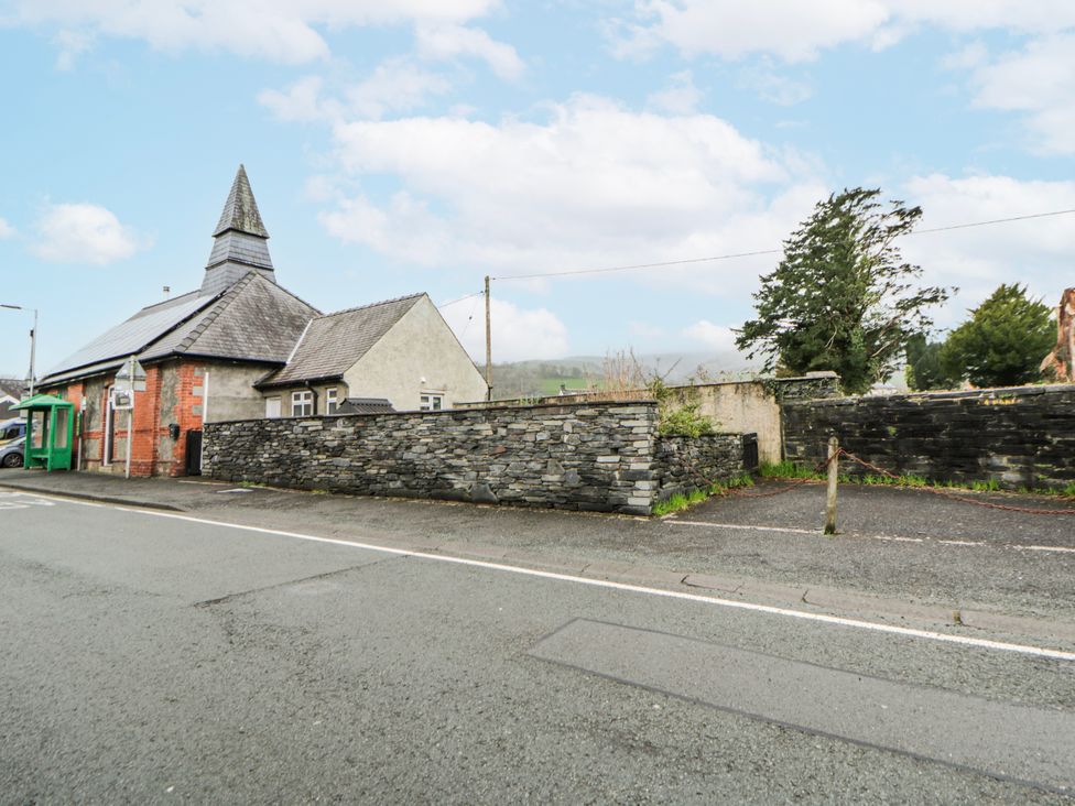A building with a spire and stone wall on a street at Yr Hen Ysgoldy