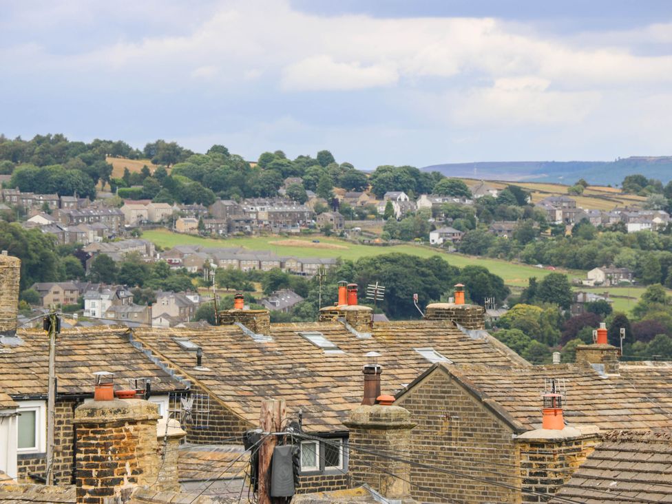 An aerial view of rooftops and houses with trees in the background at Winberry Cottage in Haworth