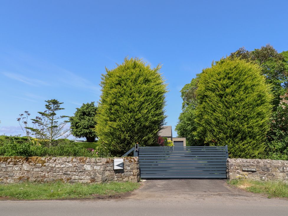 A gate and stone wall with trees at Rose Cottage in Dunstan near Embleton