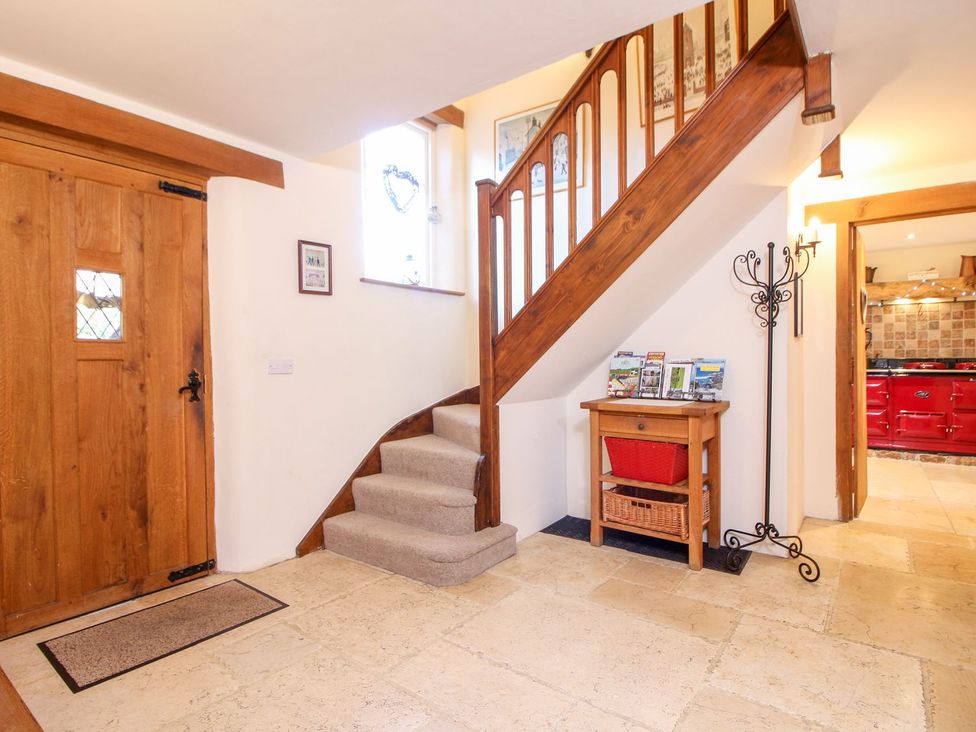 A hallway with wooden staircase and door a small table with baskets and a coat stand at Church Thatch in Abbotskerswell