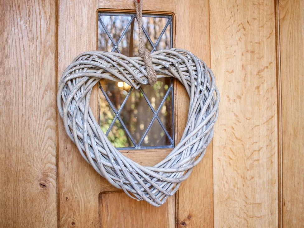 A heart-shaped wicker wreath hanging on a wooden door with a glass window at Church Thatch in Abbotskerswell