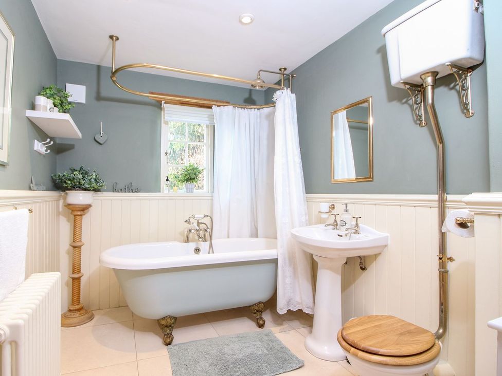 A bathroom with a clawfoot bathtub shower curtain pedestal sink and high level toilet at Church Thatch in Abbotskerswell