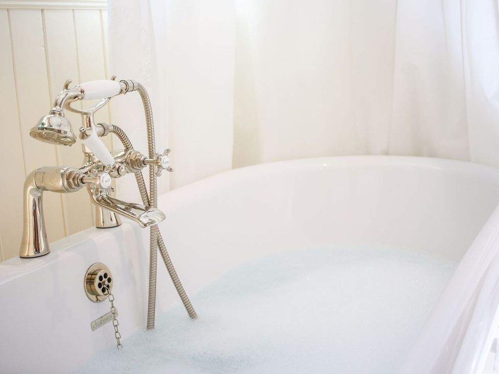 A white bathtub with a silver faucet and handheld shower head filled with water and bubbles at Church Thatch in Abbotskerswell
