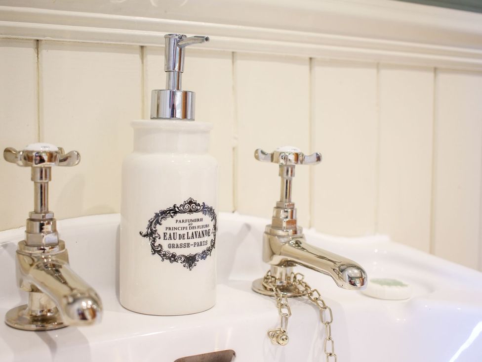 A bathroom sink with silver taps and a white soap dispenser at Church Thatch in Abbotskerswell