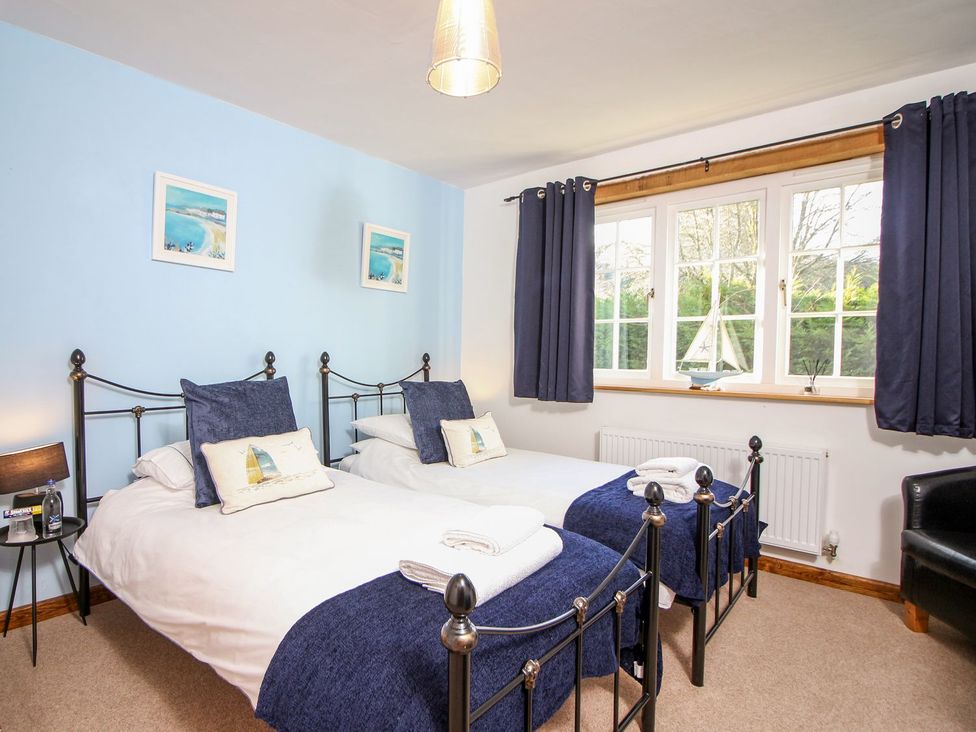 A bedroom with two single beds with blue throws and pillows and a window with dark curtains at Church Thatch in Abbotskerswell