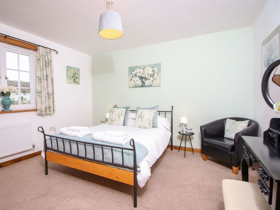 A bedroom with a double bed armchair bedside table and desk at Church Thatch in Abbotskerswell