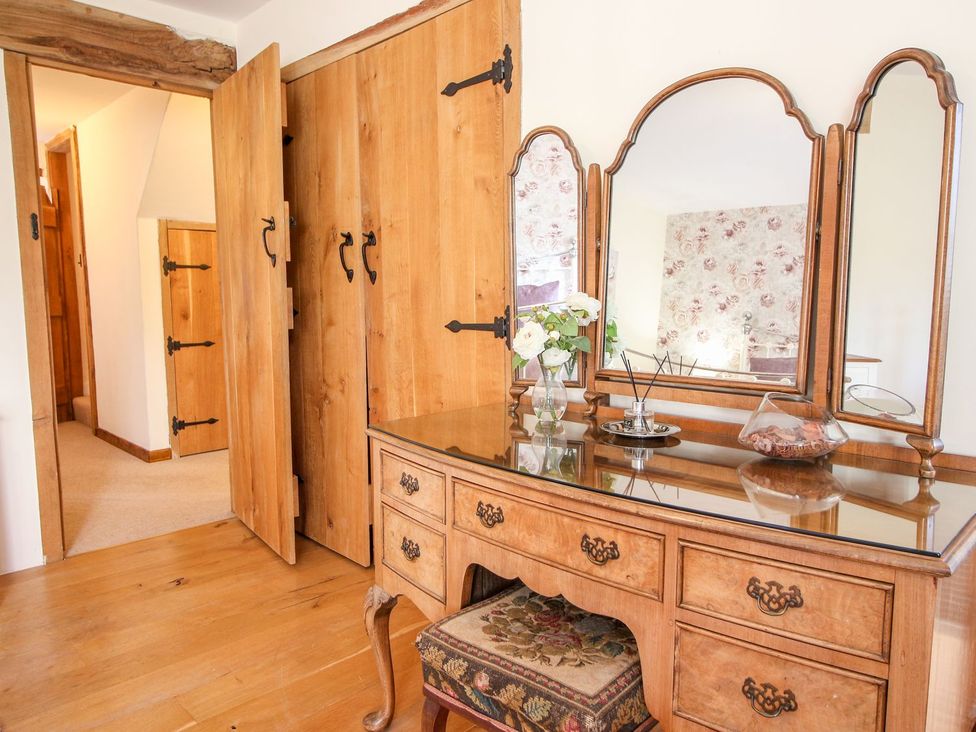A wooden dressing table with a three-paneled mirror a vase with flowers and an upholstered stool in a room at Church Thatch in Abbotskerswell