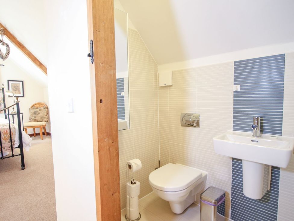 A bathroom with a wall-mounted toilet and sink next to a bedroom with a bed and chair at Church Thatch in Abbotskerswell