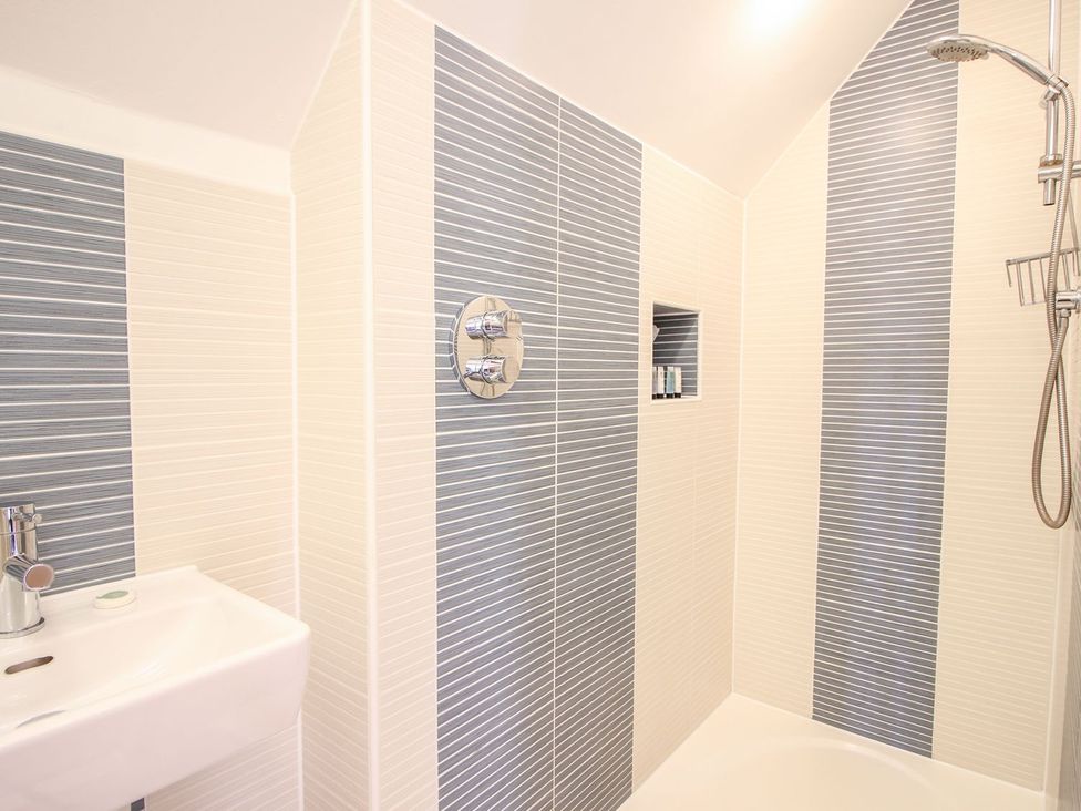 A bathroom shower area with striped wall tiles a showerhead and a small sink at Church Thatch in Abbotskerswell