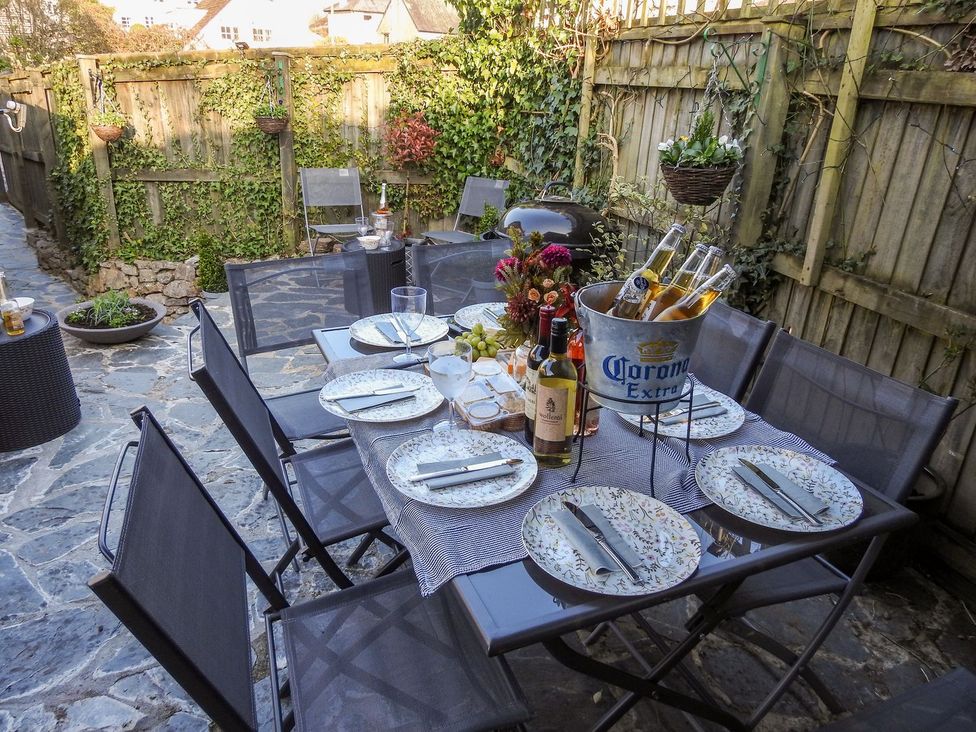 An outdoor dining area with a table set with plates knives glasses a flower centerpiece and a bucket of Corona beers at Church Thatch in Abbotskerswell
