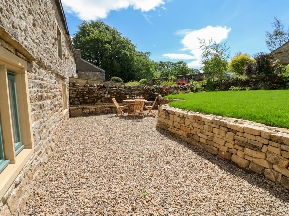 A garden area with a stone wall and a table with chairs at High Meadow Barn Thornton Rust near Bainbridge