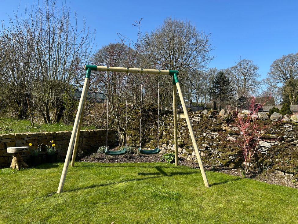 A swing set in a garden with a stone wall at High Meadow Barn Thornton Rust near Bainbridge