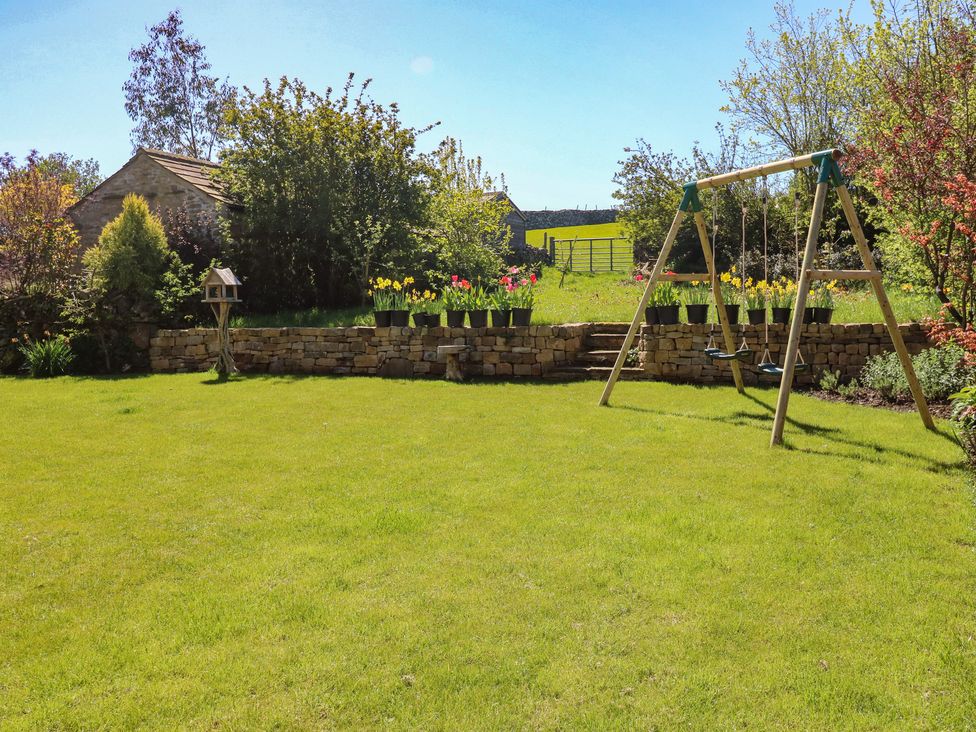 A garden with a swing set and flower pots at High Meadow Barn Thornton Rust near Bainbridge
