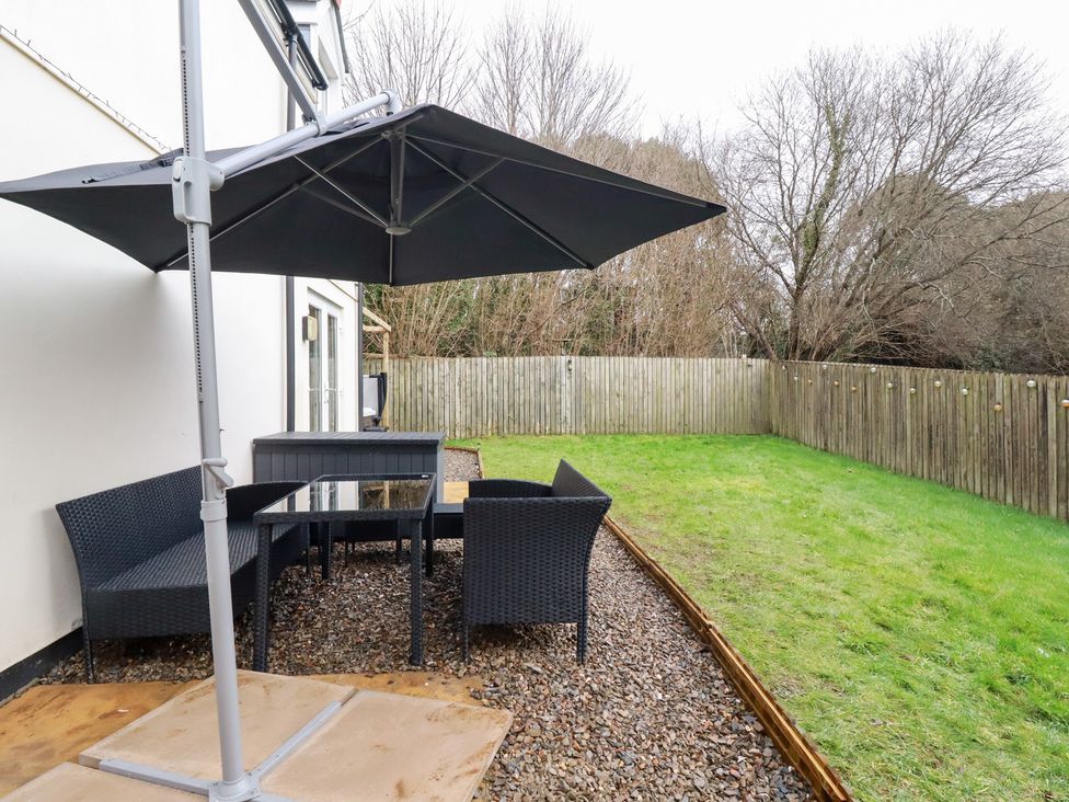 A garden with a table and chairs under a parasol at Poldam in St Austell