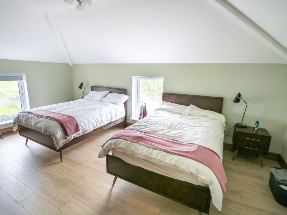 A bedroom with two beds and windows at Claddagh Tuss Holiday Cottage in Clifton