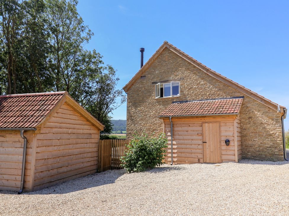 An outdoor view of a stone building and a wooden garage at The Fox Den in East Coker