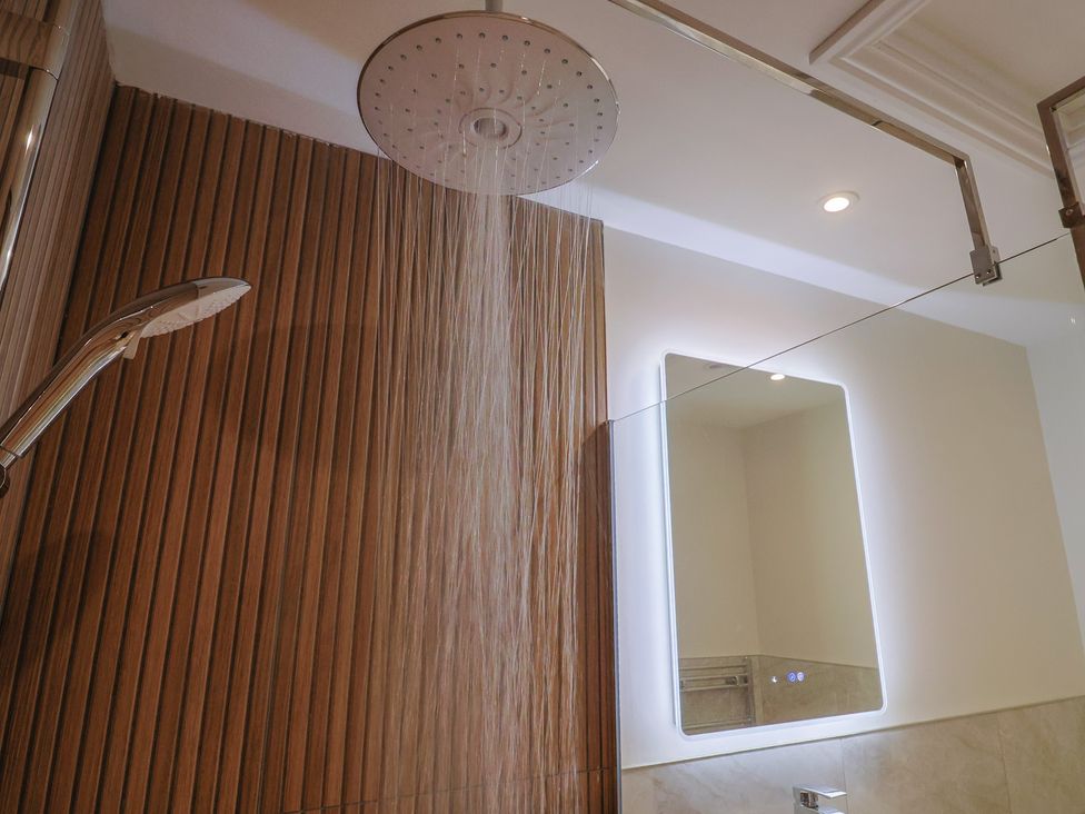 A bathroom with a shower head, handheld shower, and mirror at The Fox Den in East Coker