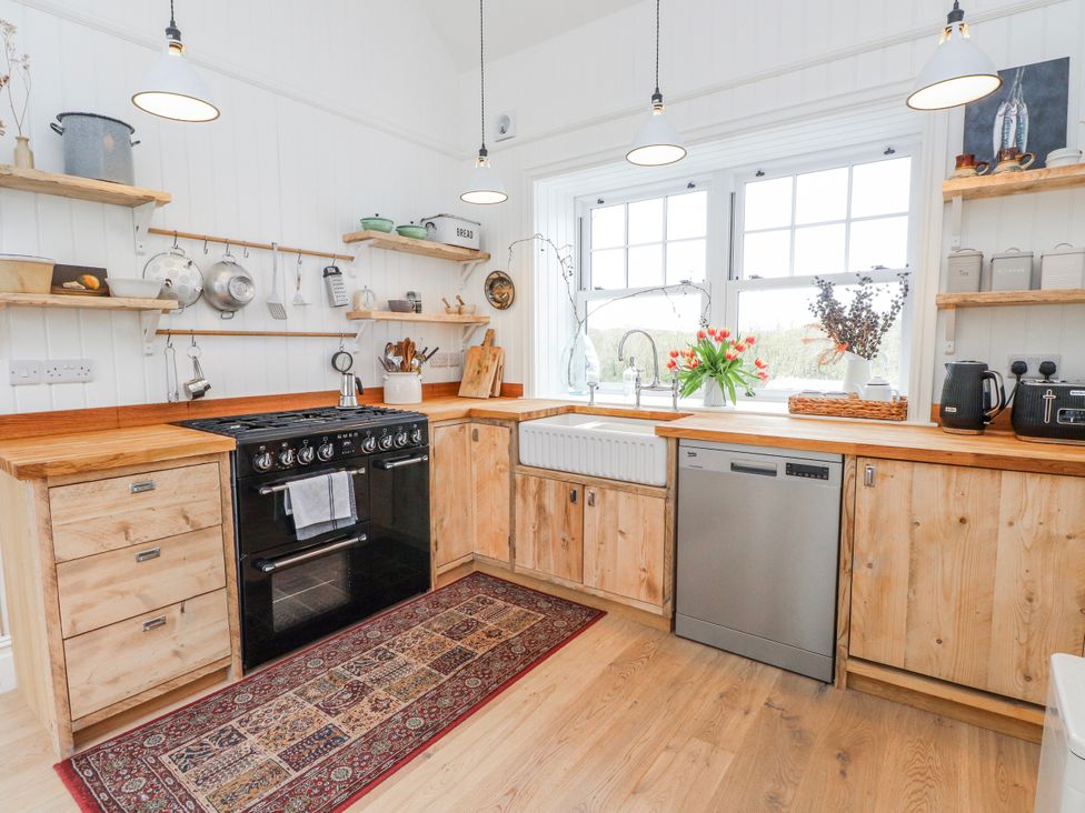 A kitchen with stove, dishwasher, and shelves at 4 bed in Anglesey