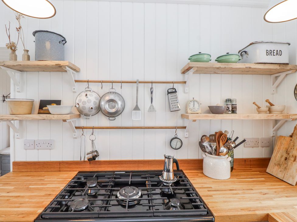 A kitchen with a gas stove and shelves holding various cooking utensils at 4 bed in Anglesey