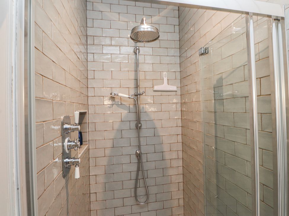 A shower with tiled wall and glass door at 4 bed in Anglesey