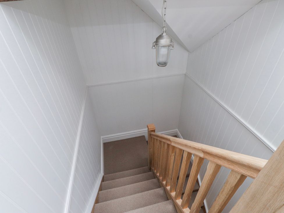 A staircase with wooden banister and light fixture at 4 bed in Anglesey