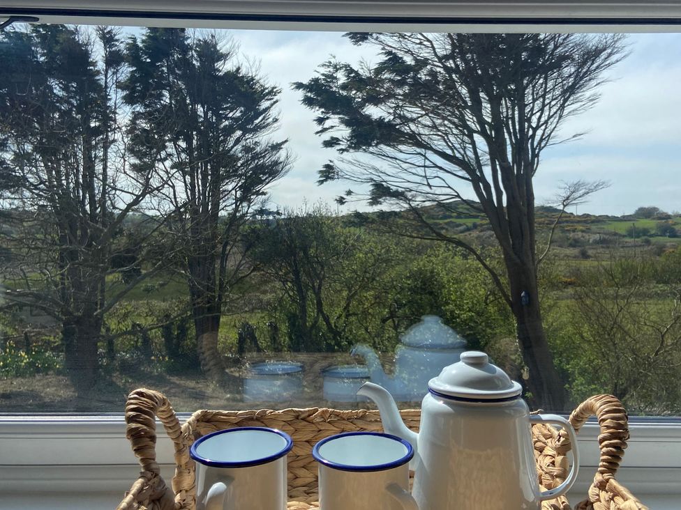 A teapot and cups on a tray with a view of trees and countryside at Arfryn Bull Bay