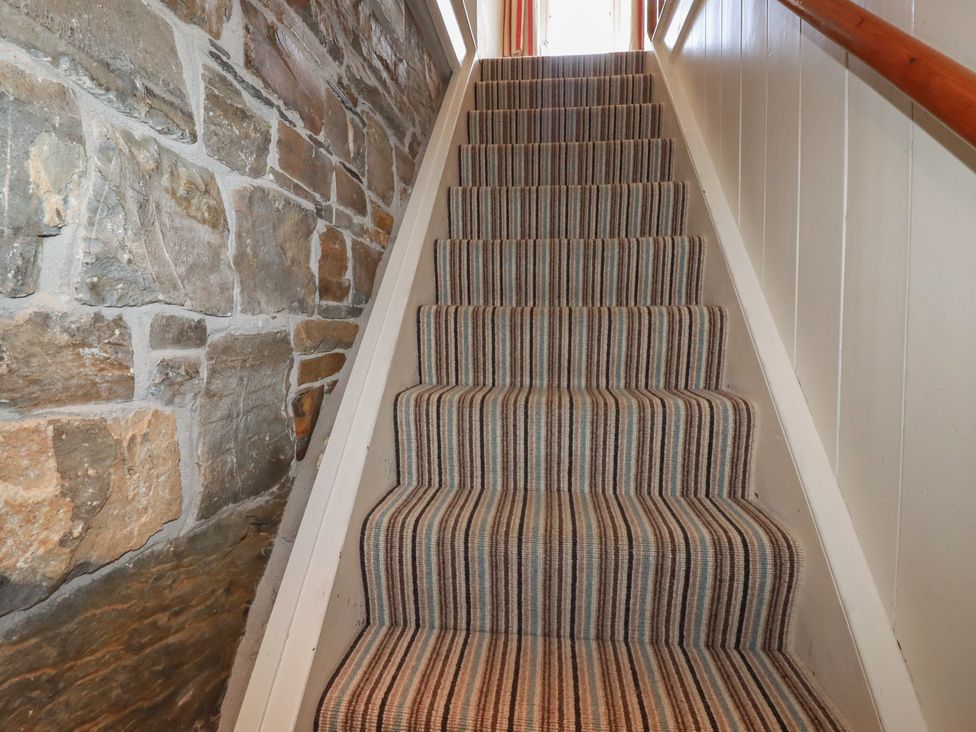 A staircase with striped carpet and stone wall at Trevean in Bude