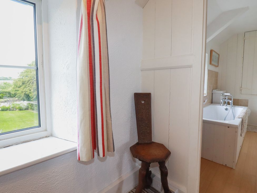 A bathroom with a window, curtain, stool and bathtub at Trevean in Bude