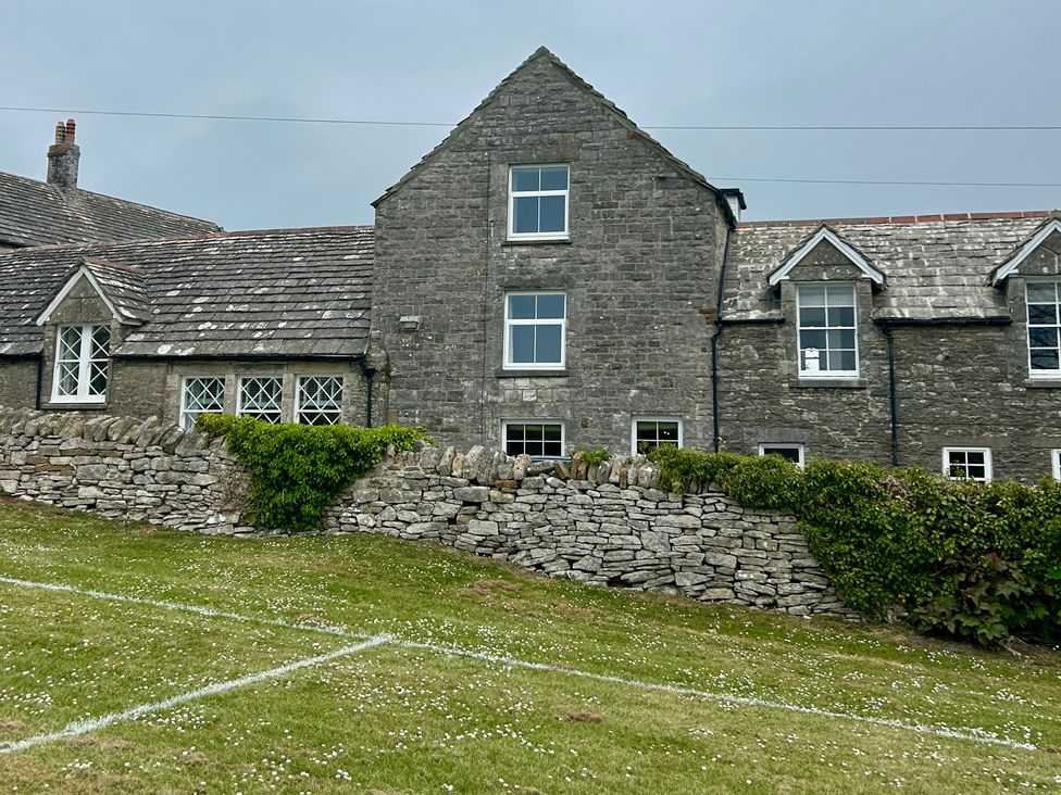 A stone house with multiple windows and a grassy area at Mallow Cottage in Langton Matravers