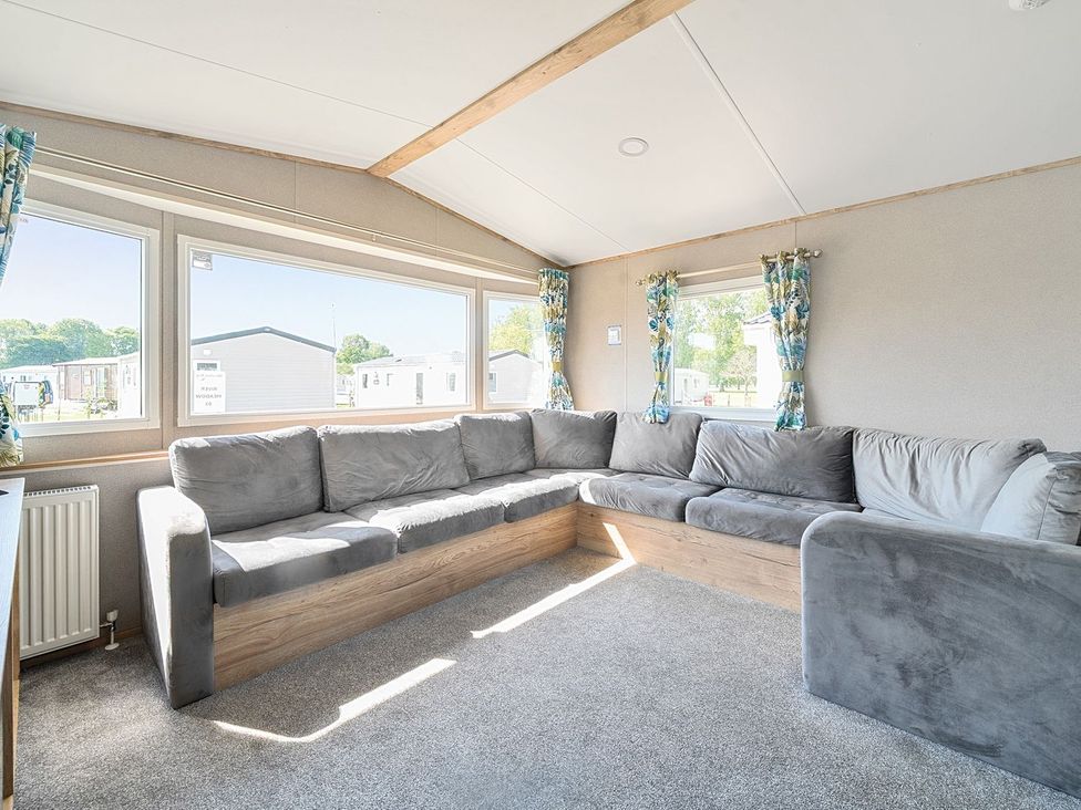 A living room with a sectional sofa and windows at Dune Delight - Hayling Island