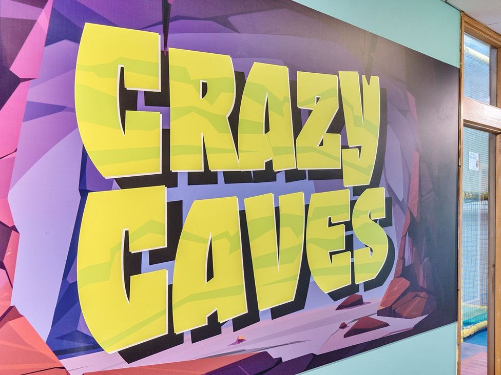 A wall with a graphic displaying 'Crazy Caves' at Dune Delight - Hayling Island Holiday Park