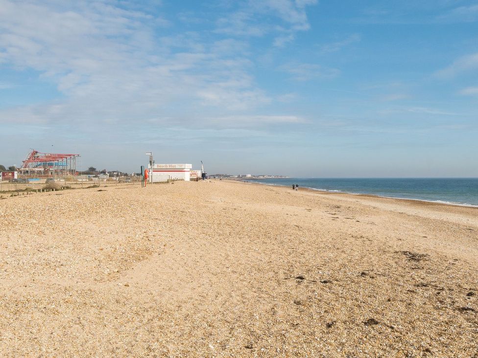 A beach with a beach hut and people walking at Dune Delight - Hayling Island